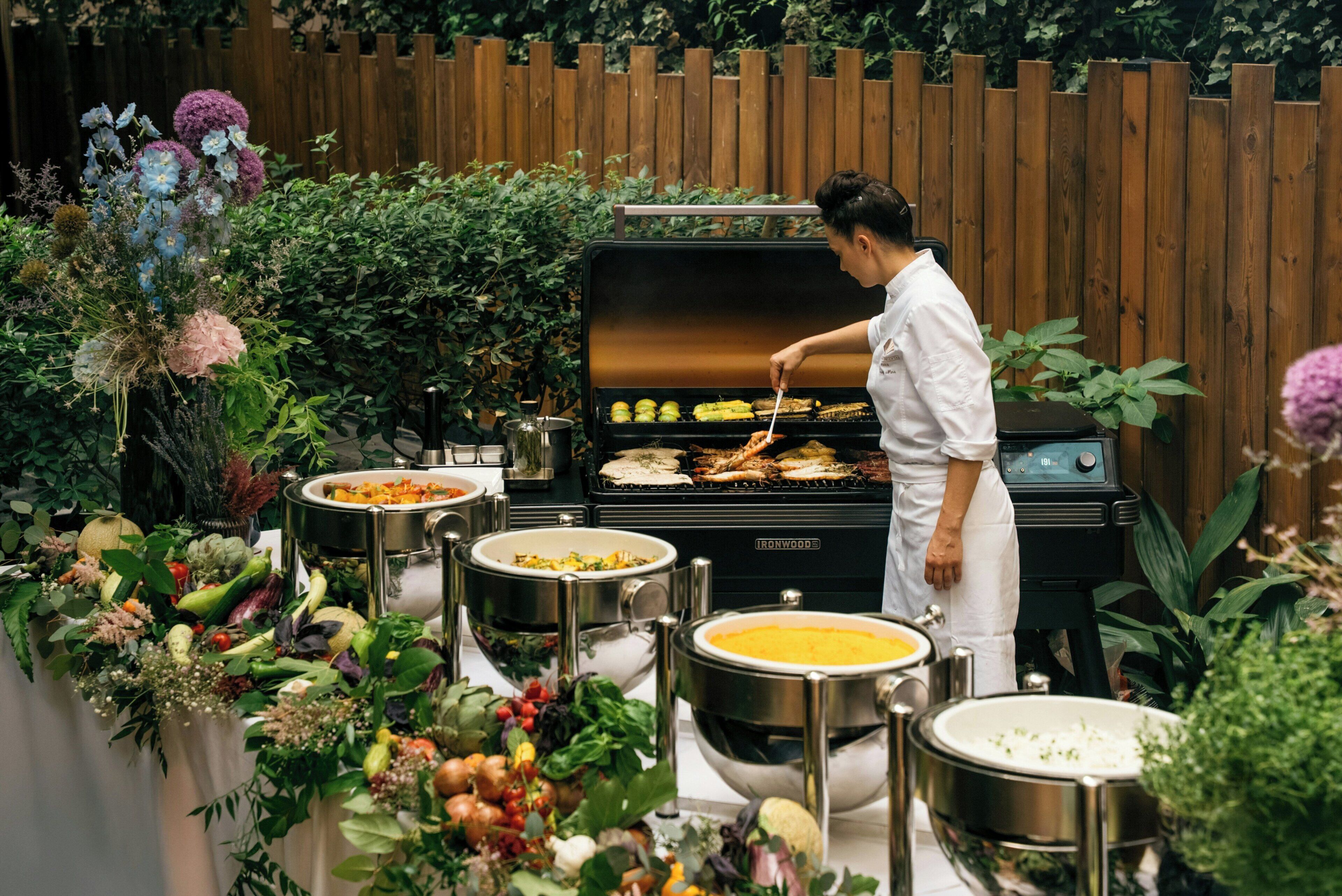 Een kok bereidt eten buiten, met diverse gerechten en een buffetopstelling.