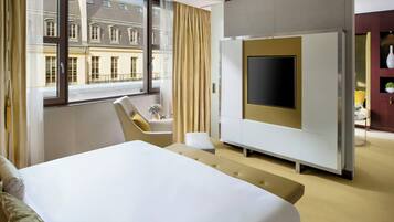 A hotel room with a large bed, a TV, a sofa, and a view of a building outside.