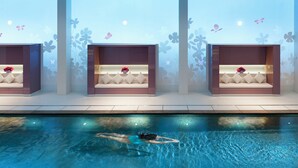 A swimming pool with a person swimming, three seating areas with cushions and flowers, and wall decorations with butterflies and flowers.