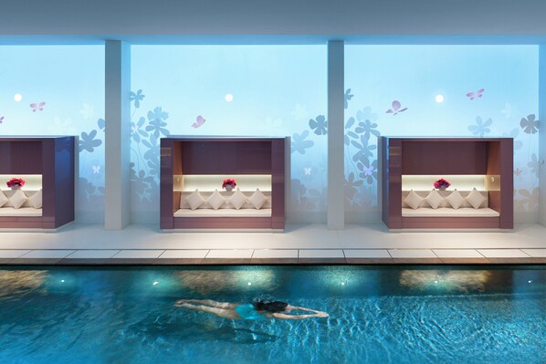 A swimming pool with a person swimming, three seating areas with cushions and flowers, and wall decorations with butterflies and flowers.