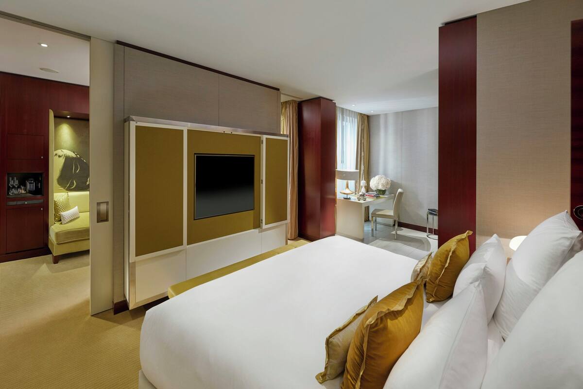 A hotel room with a large bed, a desk with a chair, a television, and a minibar.