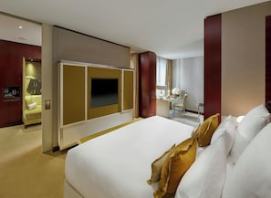 A hotel room with a large bed, a desk with a chair, a television, and a minibar.