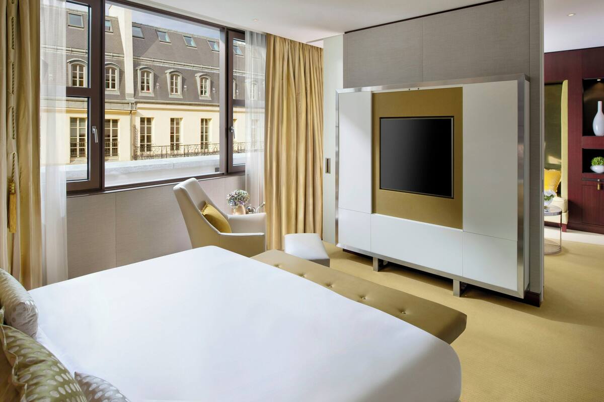 A hotel room with a large bed, a TV, a sofa, and a view of a building outside.