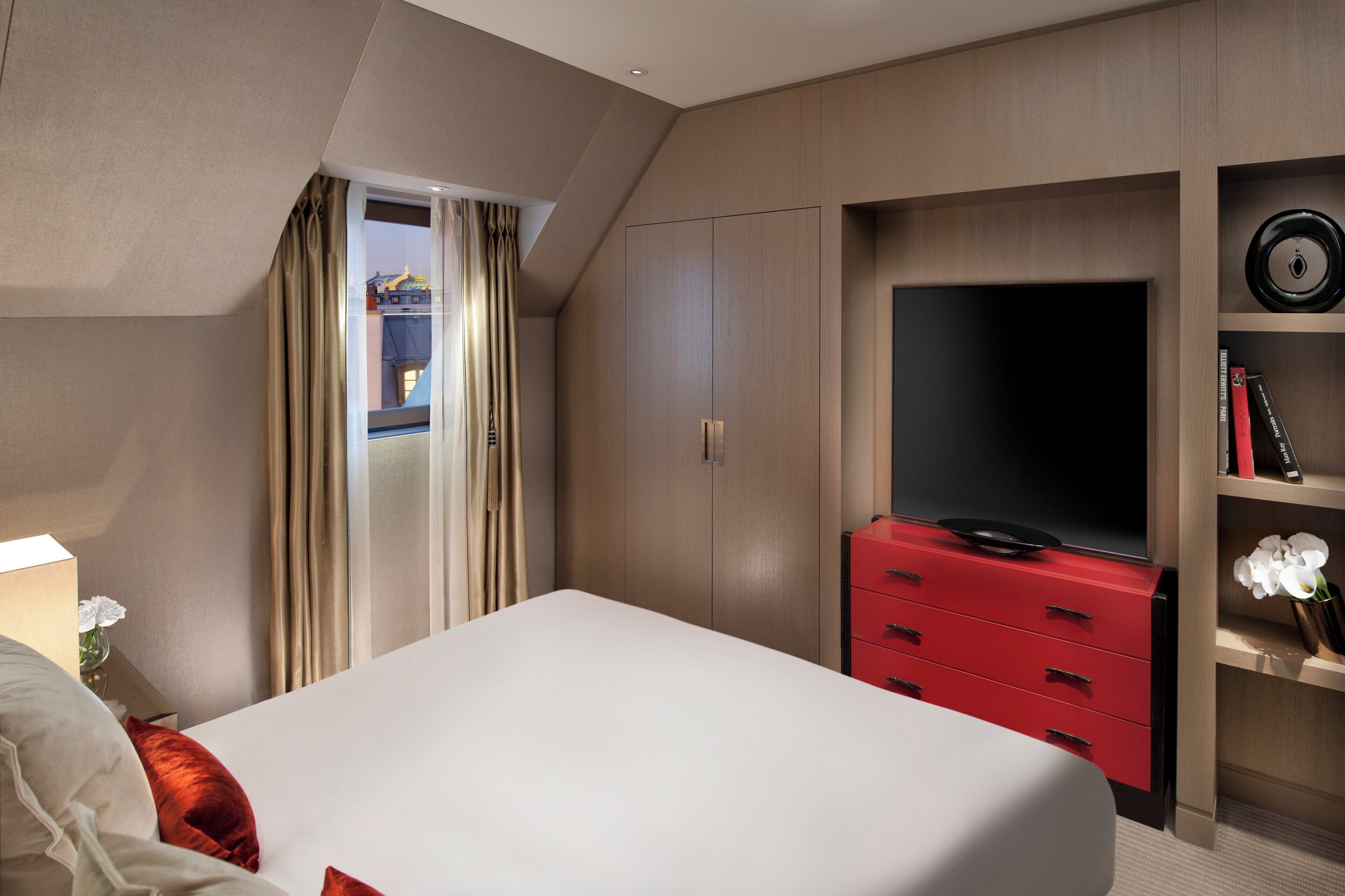 A hotel room with a bed, a TV, a red dresser, and a wardrobe.
