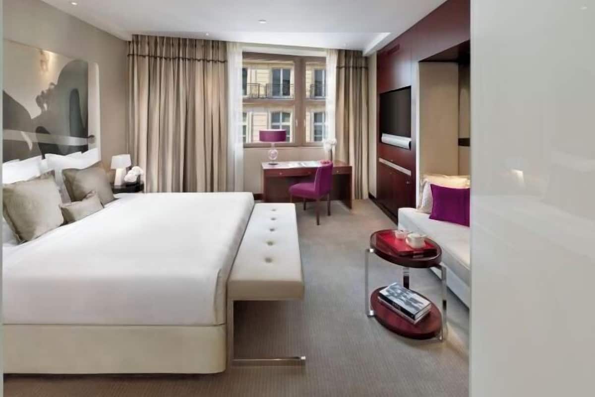 A hotel room with a large bed, a desk, a chair, a TV, and a small table with a tray.