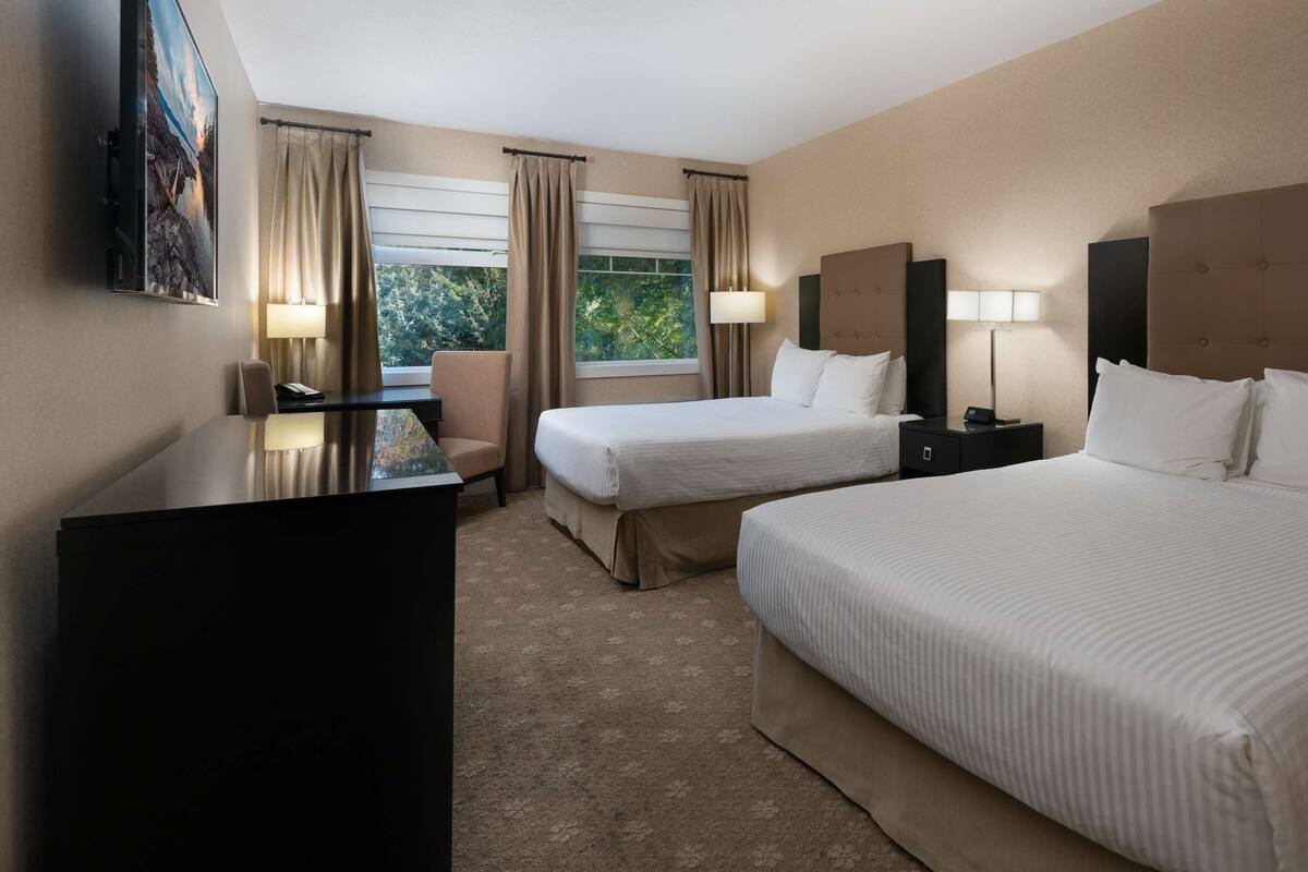 Quarto de hotel com duas camas, uma mesa, uma cadeira e uma televisão.