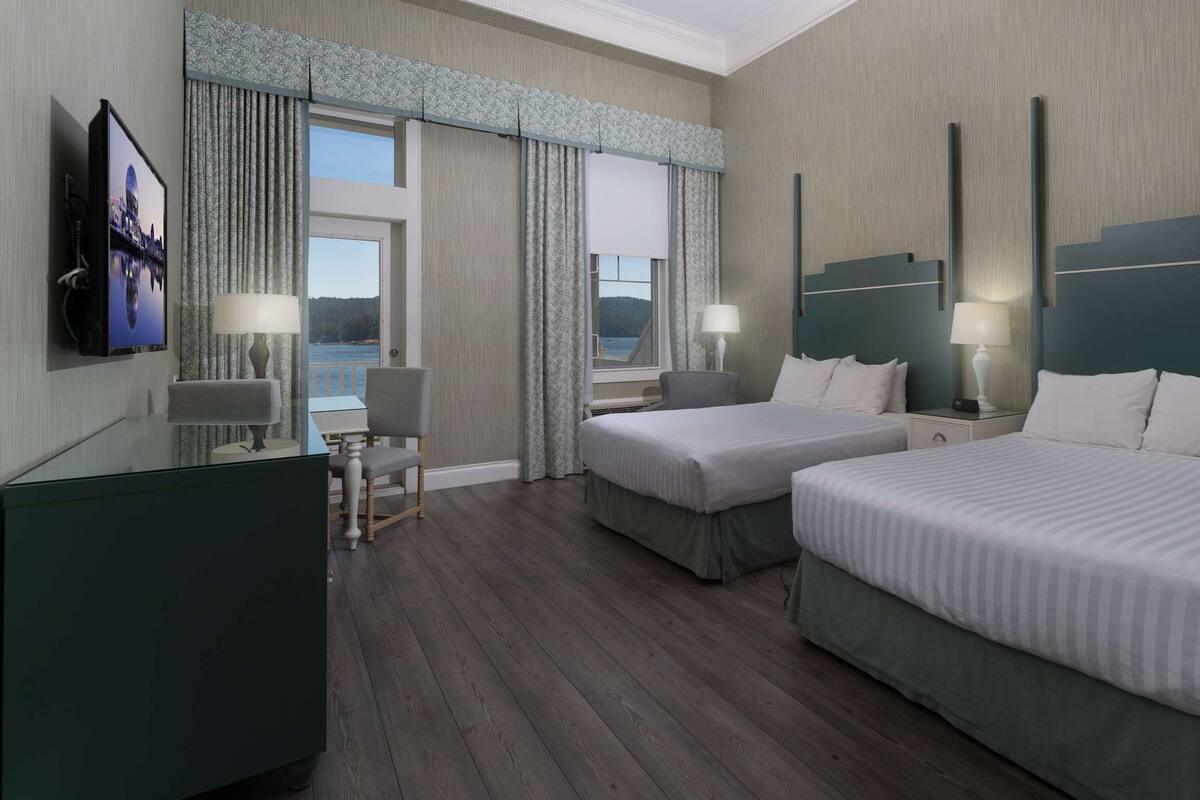 Quarto de hotel com duas camas, uma escrivaninha, uma cadeira e uma televisão.