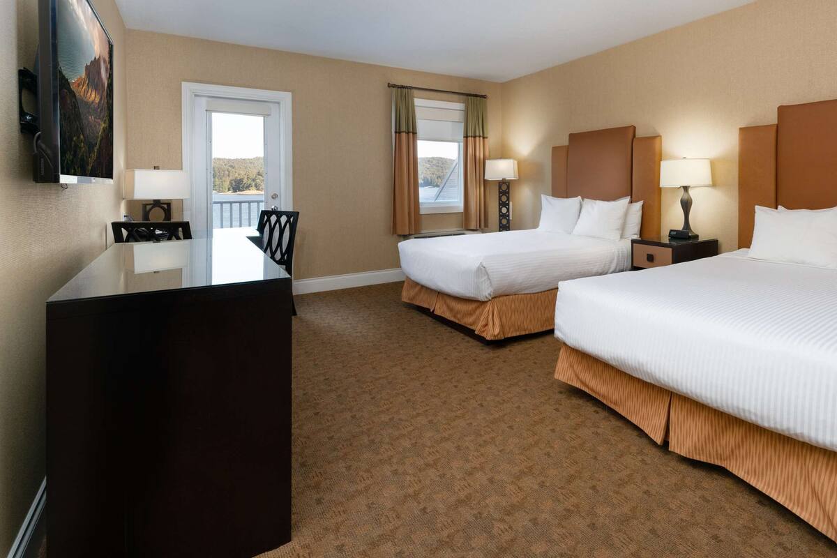 Quarto de hotel com duas camas, uma escrivaninha, televisão e varanda com vista.