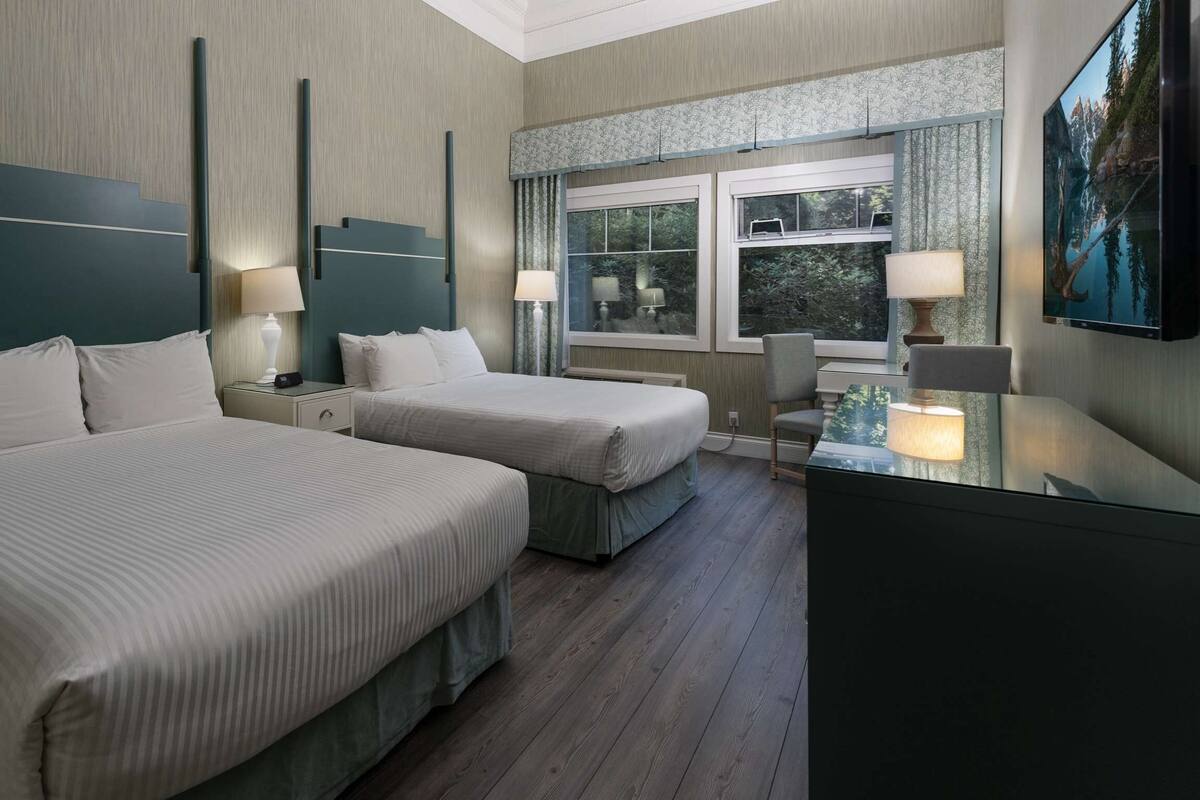 Quarto de hotel com duas camas, uma escrivaninha e uma televisão.