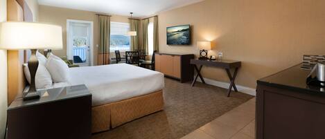 A hotel room with a large bed, a desk, a chair, a lamp, and a view of the outdoors.