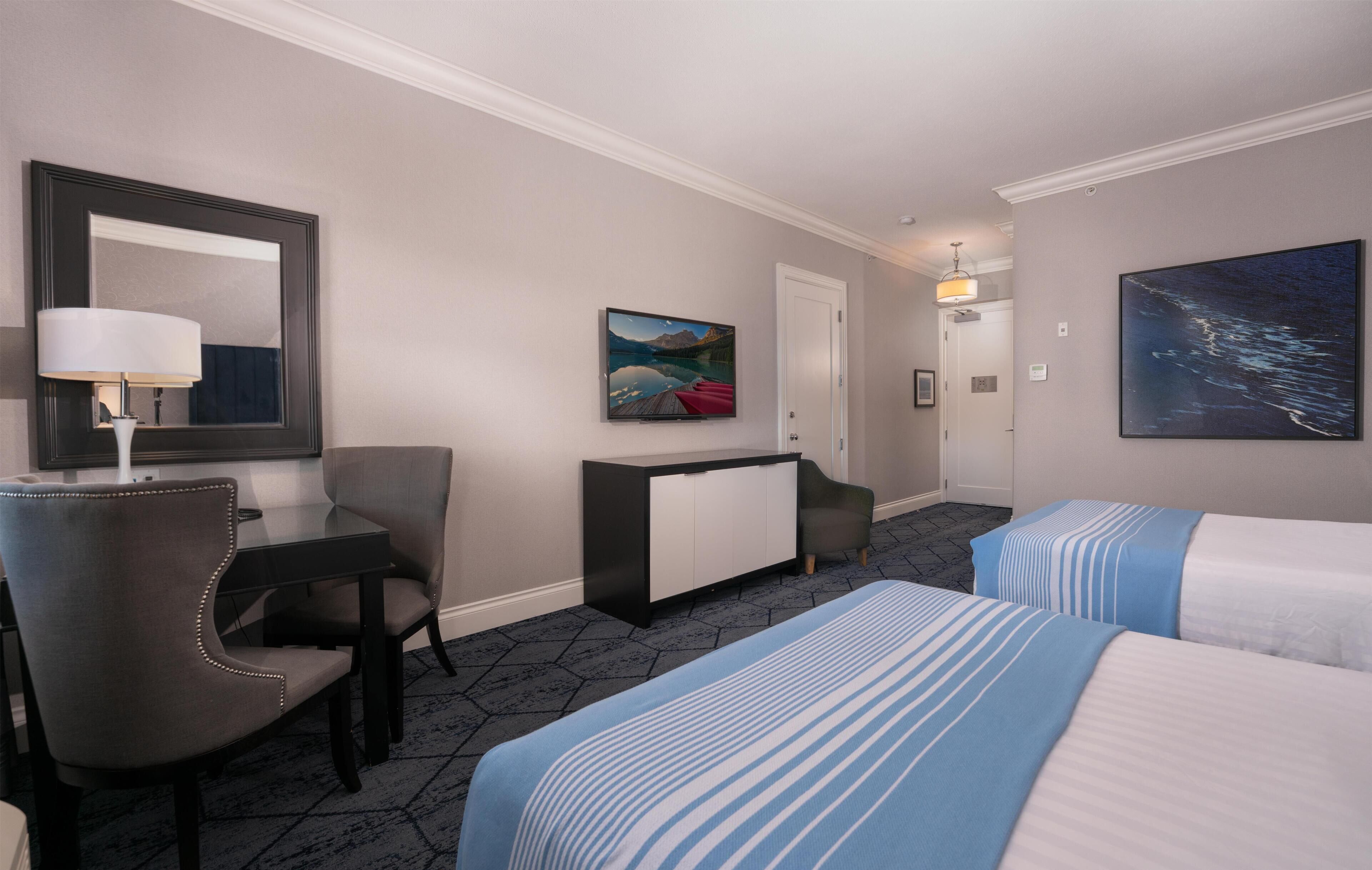 Une chambre d’hôtel avec un lit, un bureau, une chaise, une commode, un tableau et une porte.