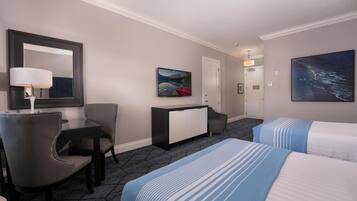 Une chambre d’hôtel avec un lit, un bureau, une chaise, une commode, un tableau et une porte.