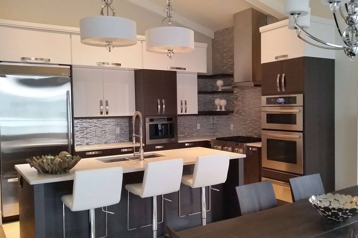 Uma cozinha moderna com eletrodomésticos de aço inoxidável, uma ilha central com banquetas e iluminação pendente.