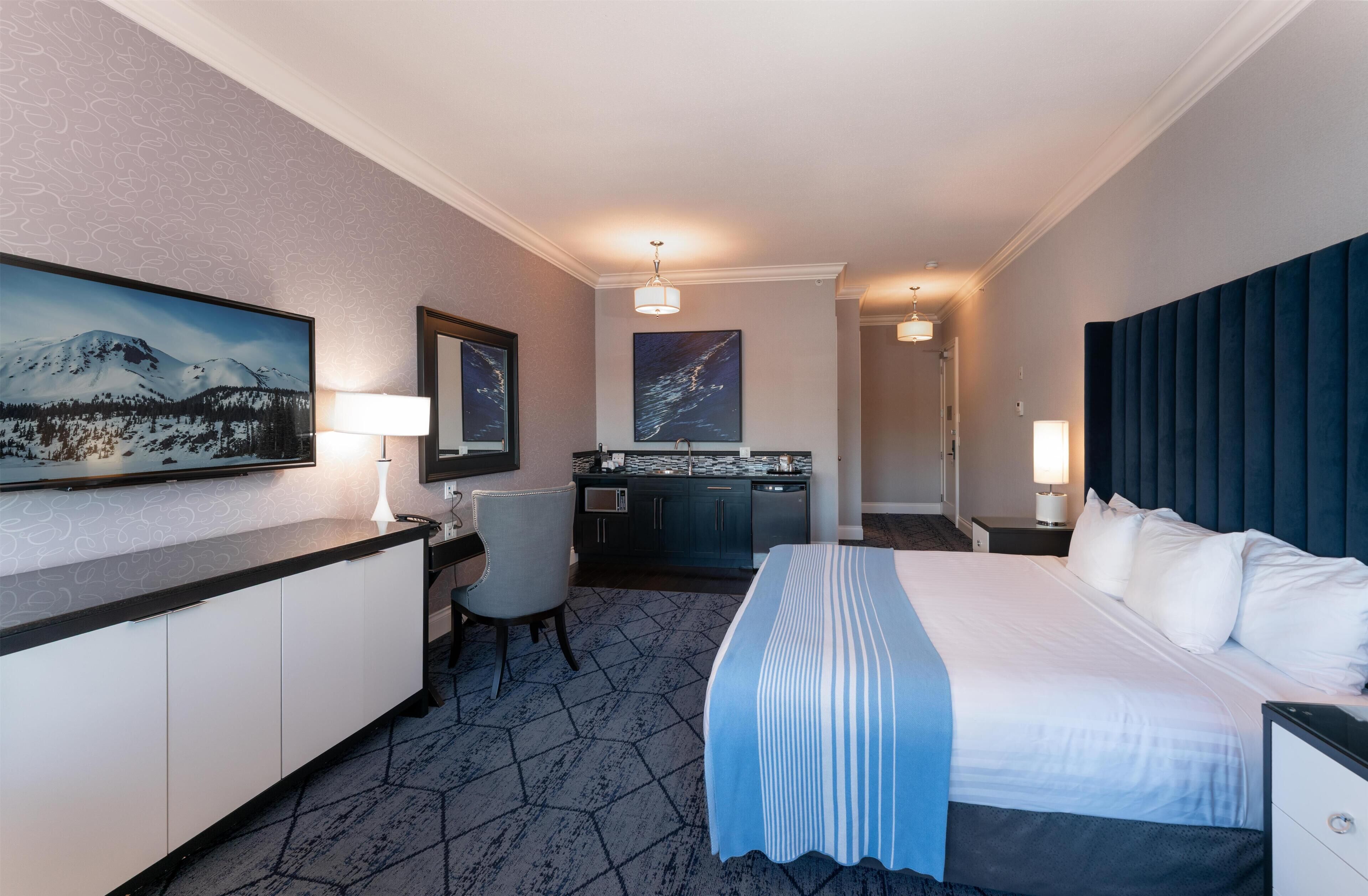 A hotel room with a bed, desk, chair, and artwork on the walls.