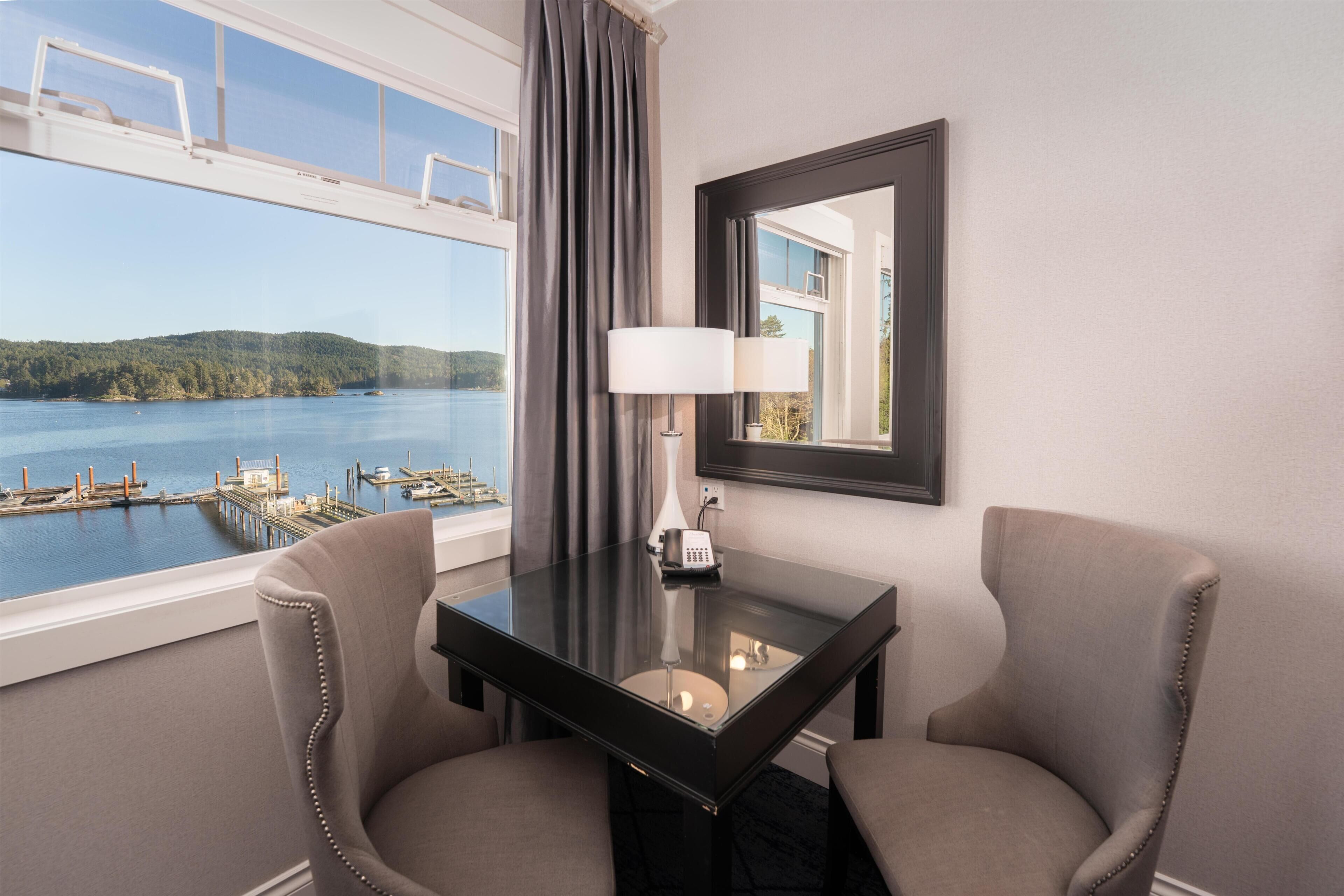 Een hotelkamer met uitzicht op een waterpartij, een tafel met stoelen, een lamp en een telefoon.