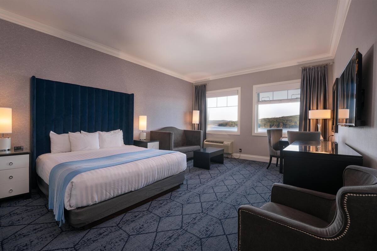Quarto de hotel com uma cama grande, uma escrivaninha, uma cadeira e vista para o exterior.