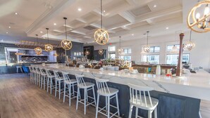 A modern bar area with a long counter, white bar stools, and pendant lighting. - Prestige Oceanfront Resort, WorldHotels Luxury (Sooke)