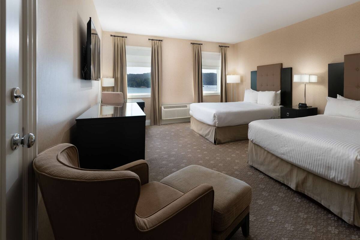 Quarto de hotel com duas camas, uma escrivaninha, uma cadeira e uma televisão.