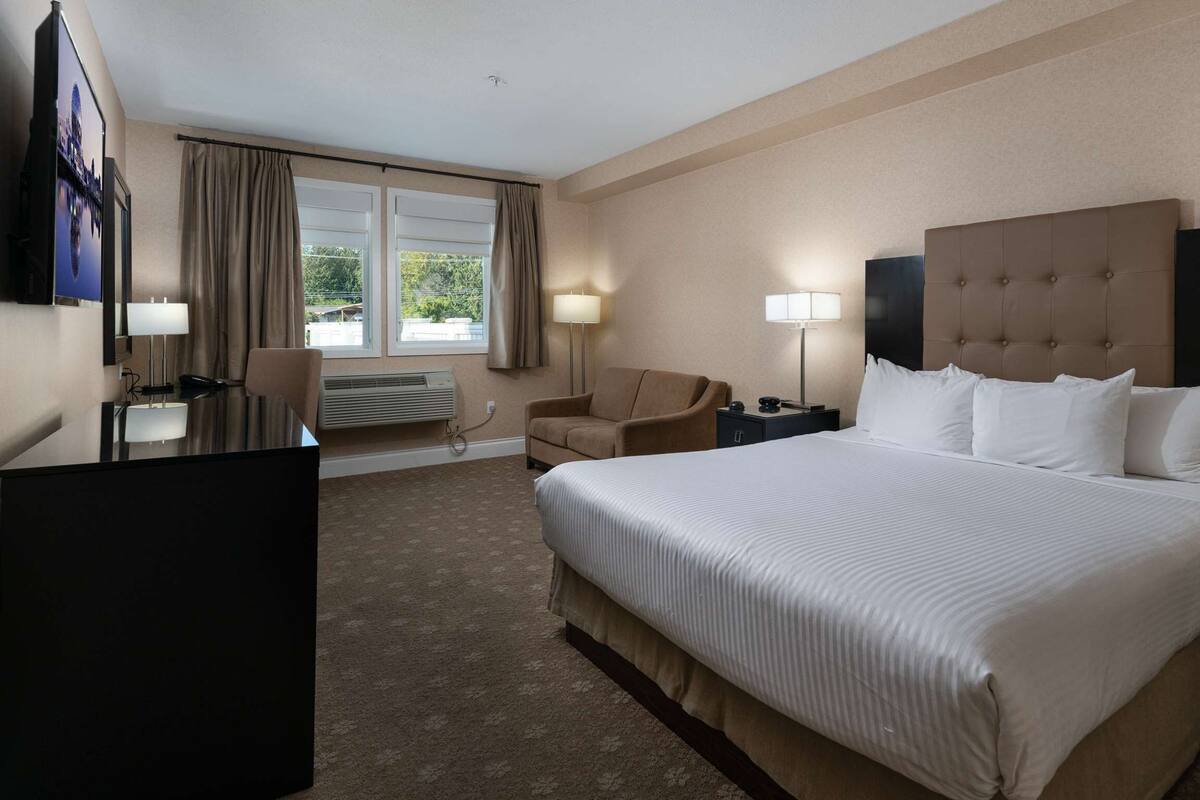 Quarto de hotel com uma cama grande, uma escrivaninha, uma cadeira e uma televisão.