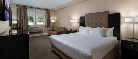 A hotel room with a large bed, a desk, a chair, and a TV.