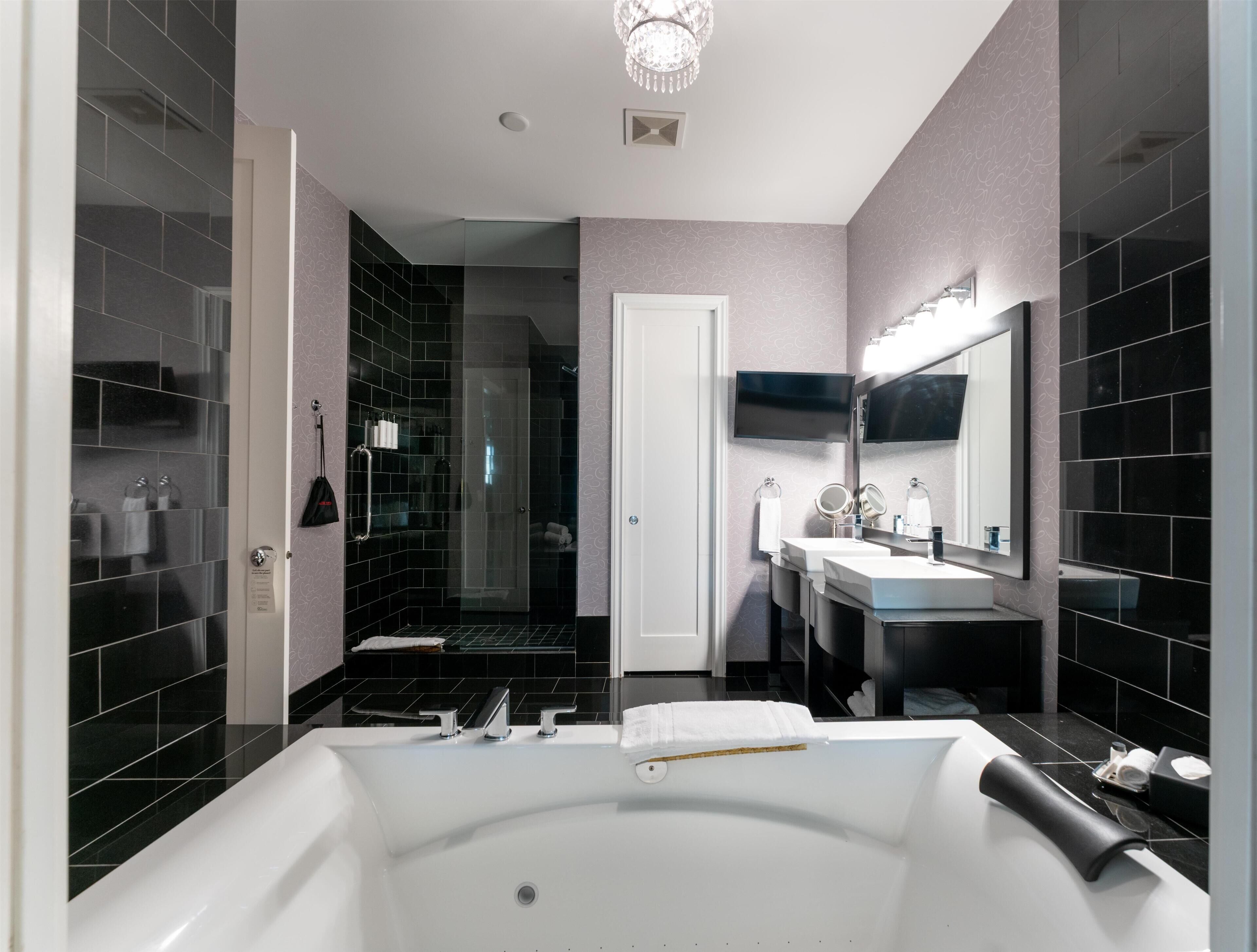 A modern bathroom with a large bathtub, two sinks, a shower area, and a mirror.
