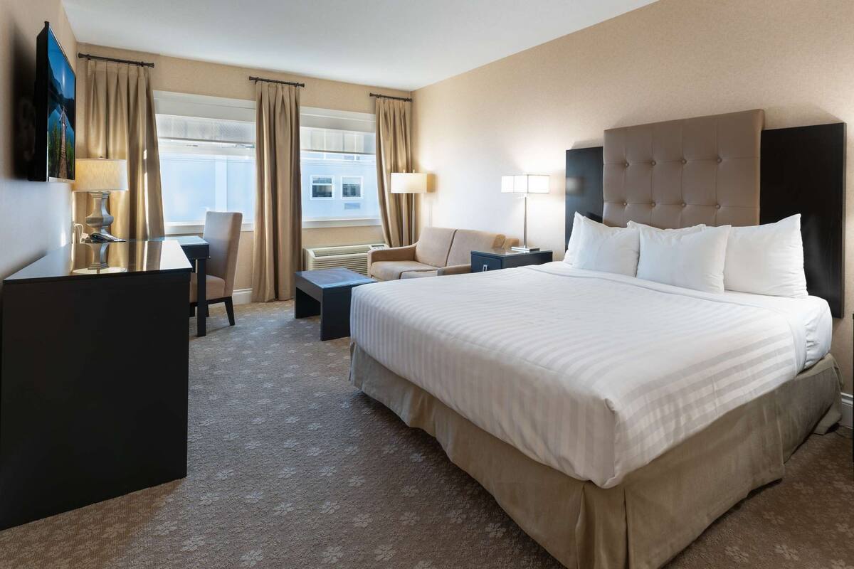 Quarto de hotel com uma cama grande, uma escrivaninha, uma cadeira e uma televisão.