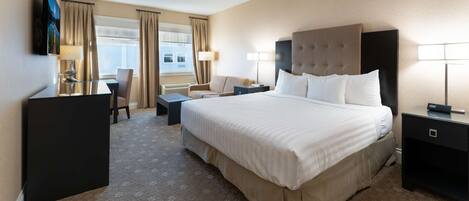 A hotel room with a large bed, a desk, a chair, and a TV.