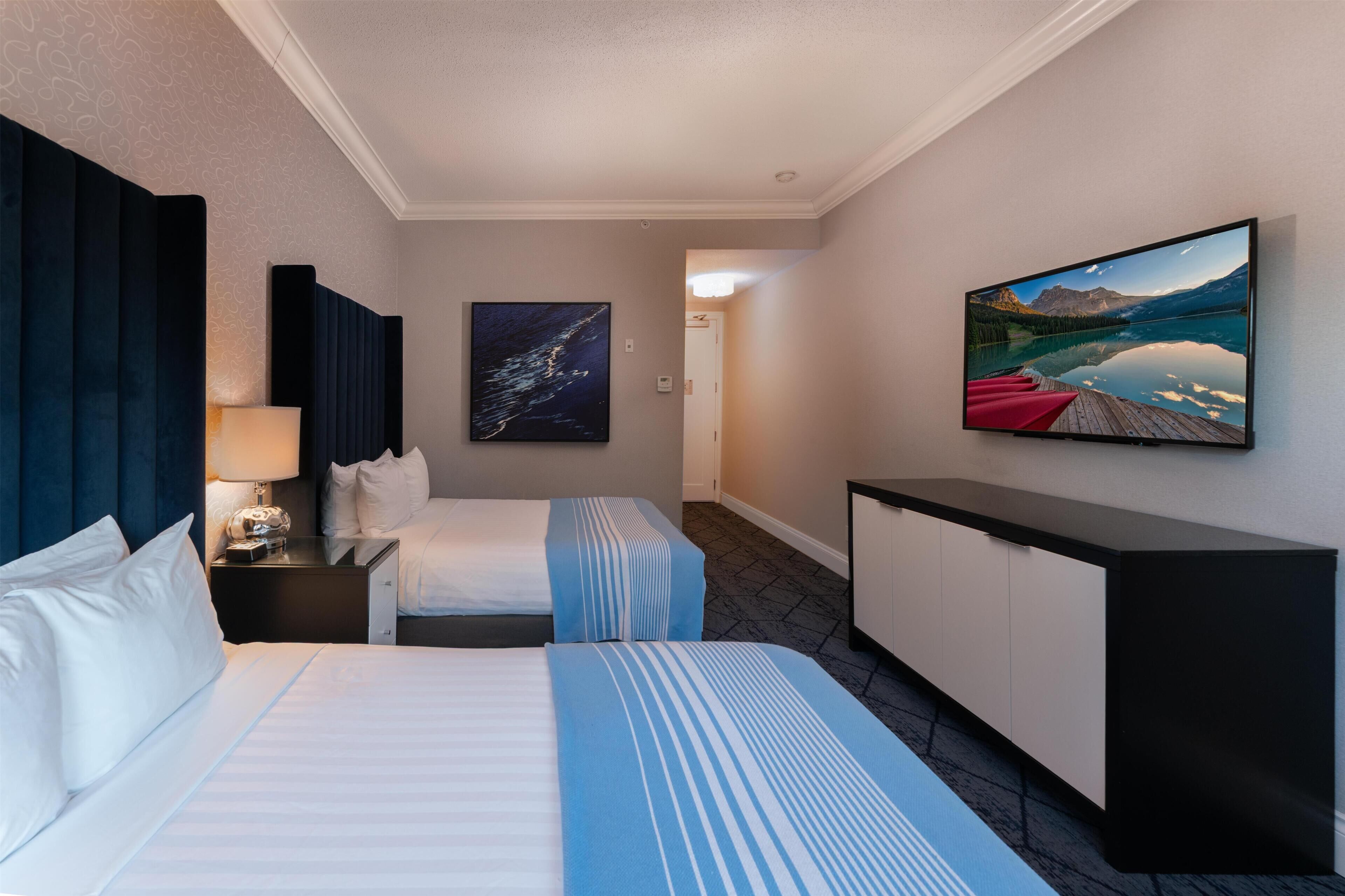 A hotel room with two beds, a flat-screen TV, a painting, and a desk.
