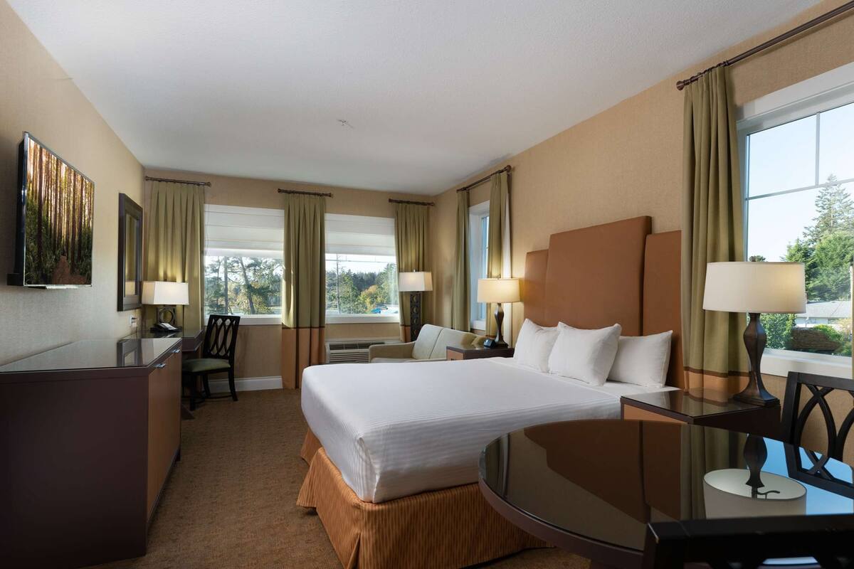 Quarto de hotel com uma cama grande, uma escrivaninha, uma cadeira e uma janela com cortinas.