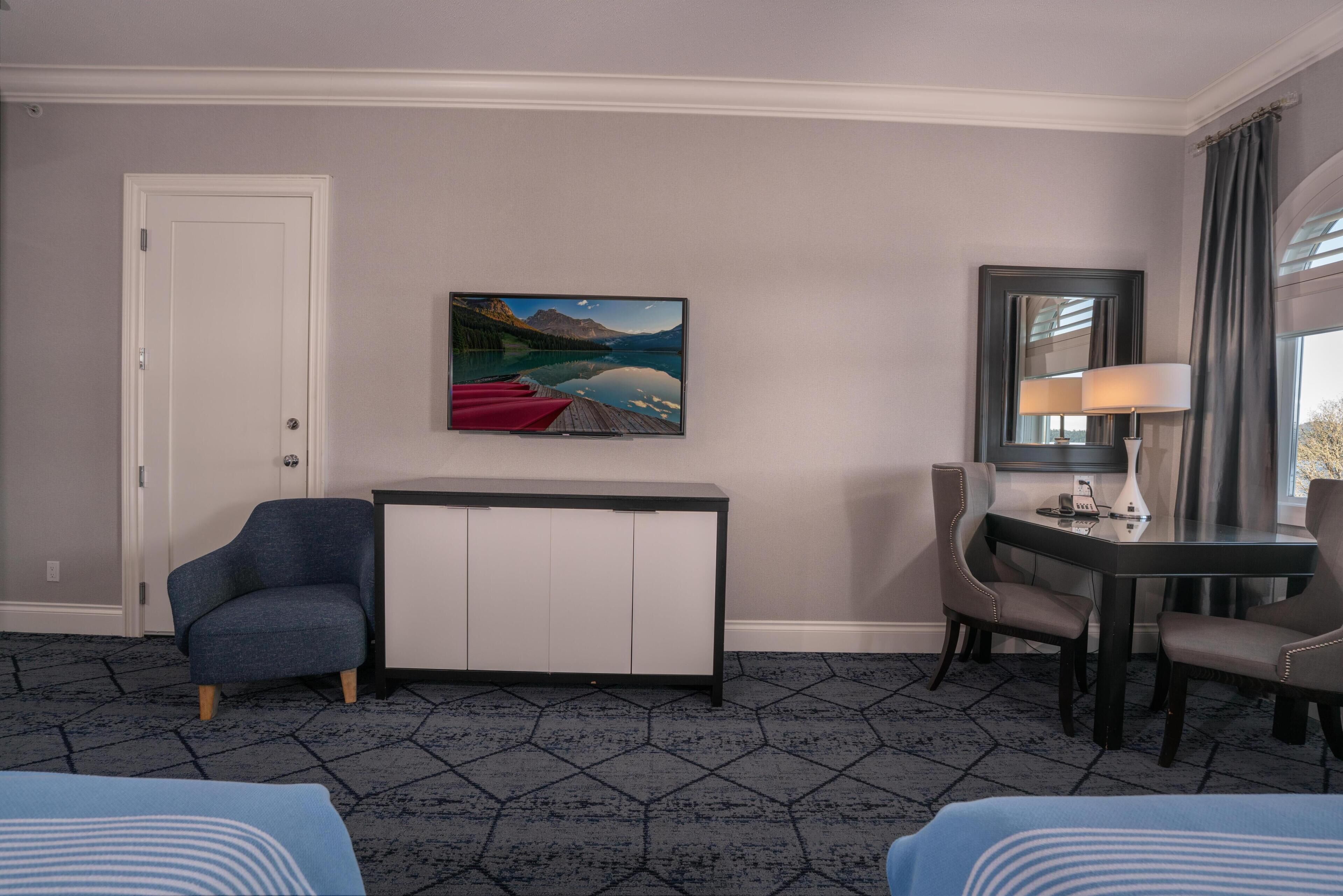 Habitación de hotel con cama, escritorio, silla, televisión y un cuadro en la pared.