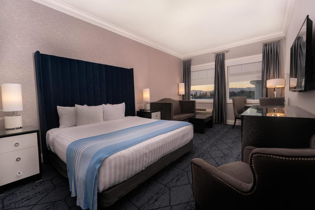 Quarto de hotel com uma cama grande, uma escrivaninha, uma cadeira e vista para a paisagem urbana.