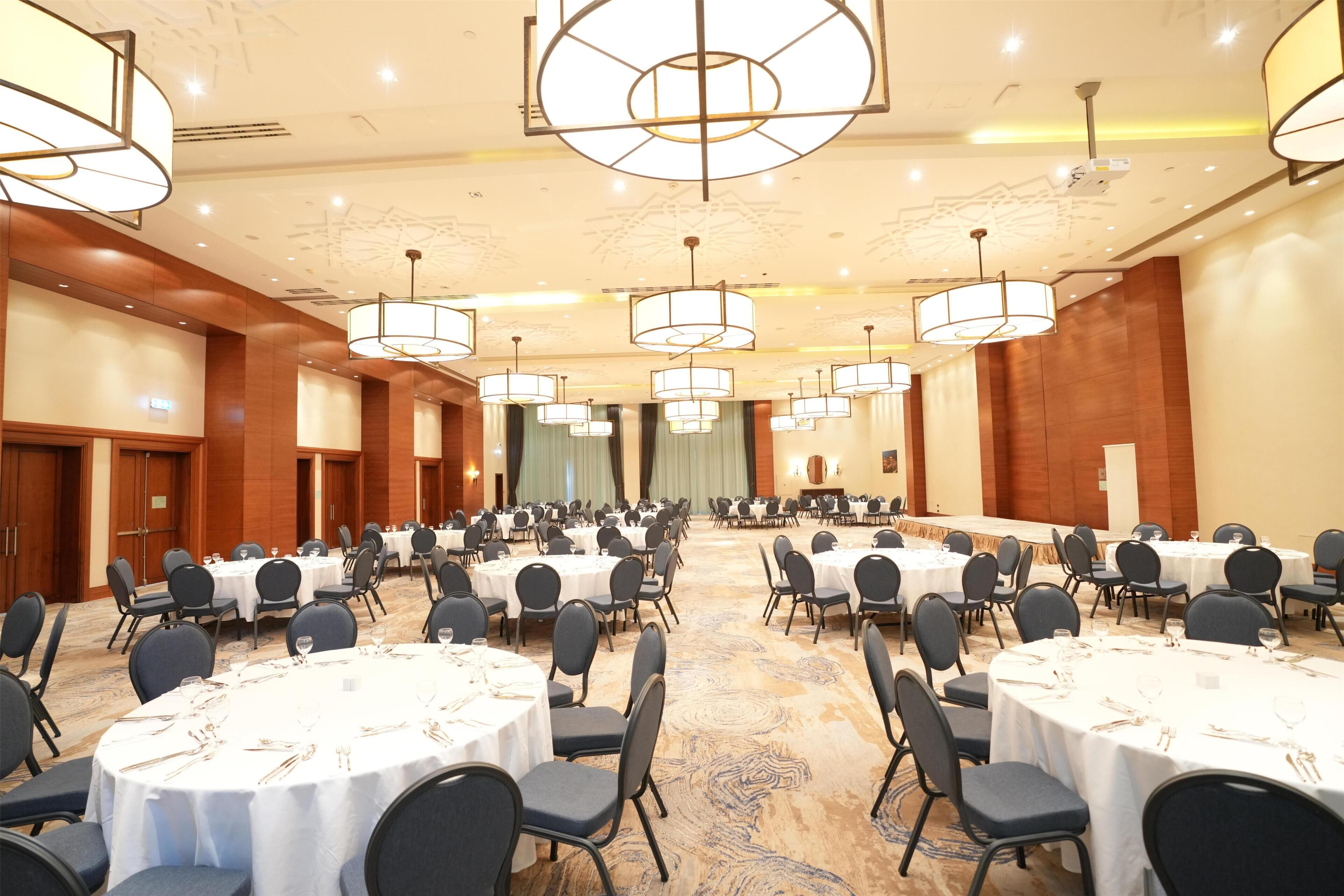 A large conference room with multiple round tables, each set with chairs and tableware.