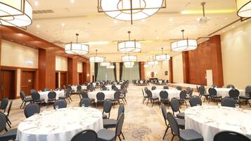 A large conference room with multiple round tables, each set with chairs and tableware.