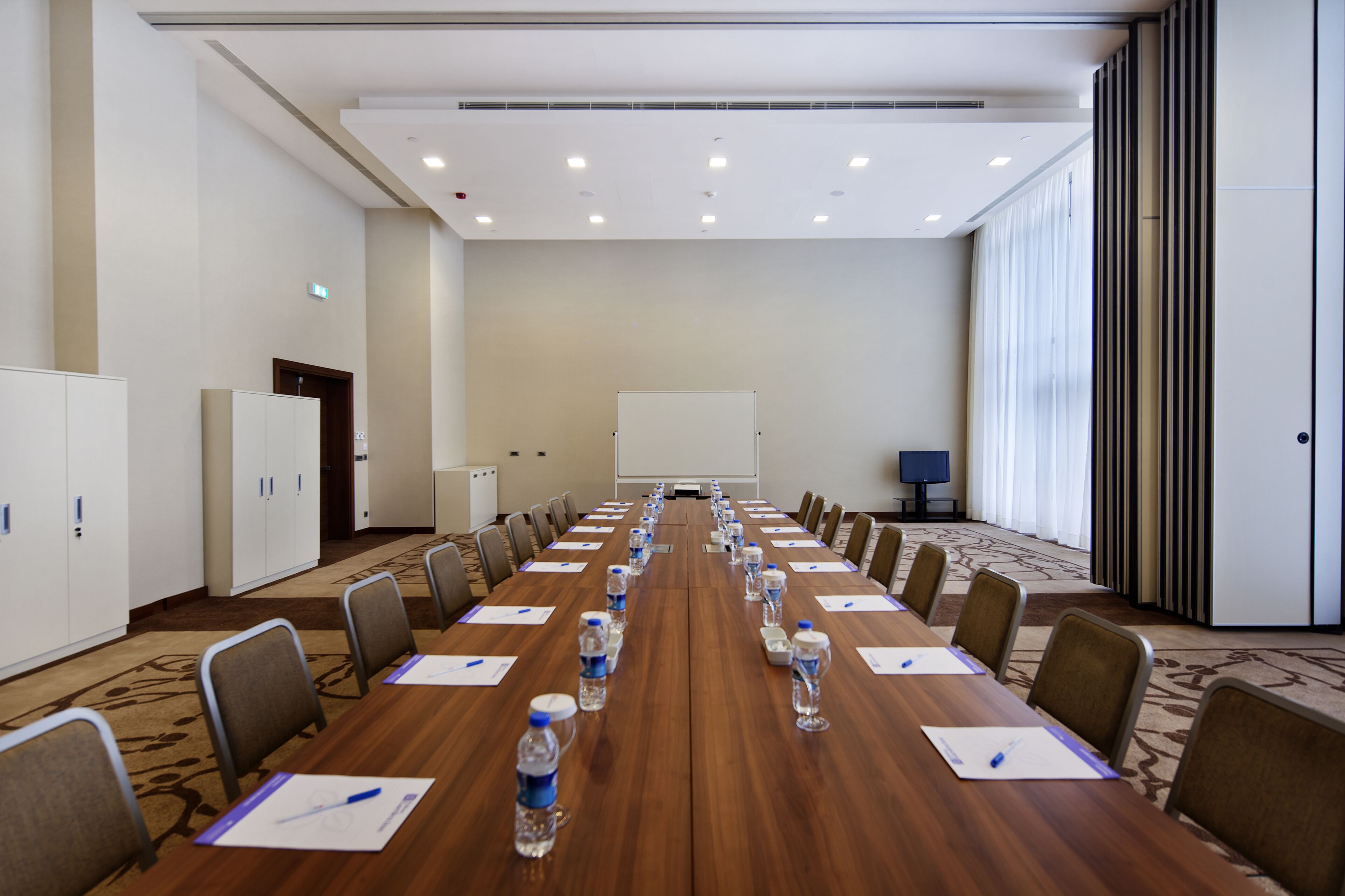 A conference room with a long table, chairs, water bottles, and a projector screen.