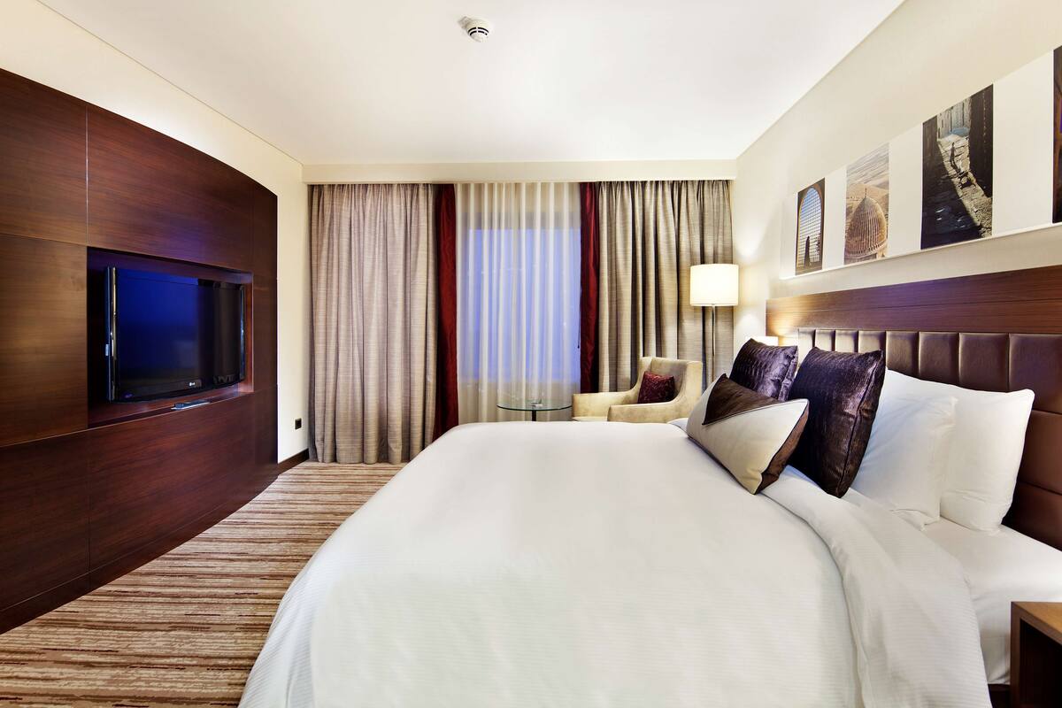 A hotel room with a large bed, a television, a small table, and a chair.