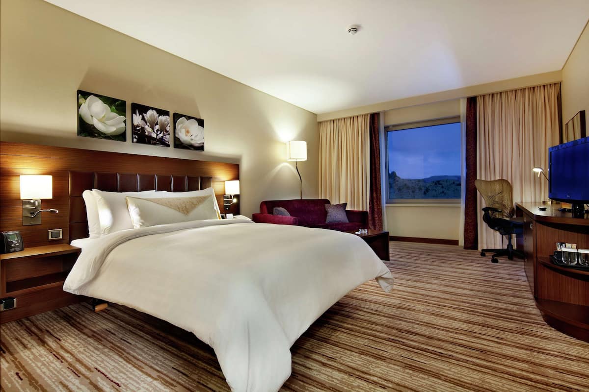 A hotel room with a large bed, a red sofa, a desk with a computer, and a window with a view of the mountains.