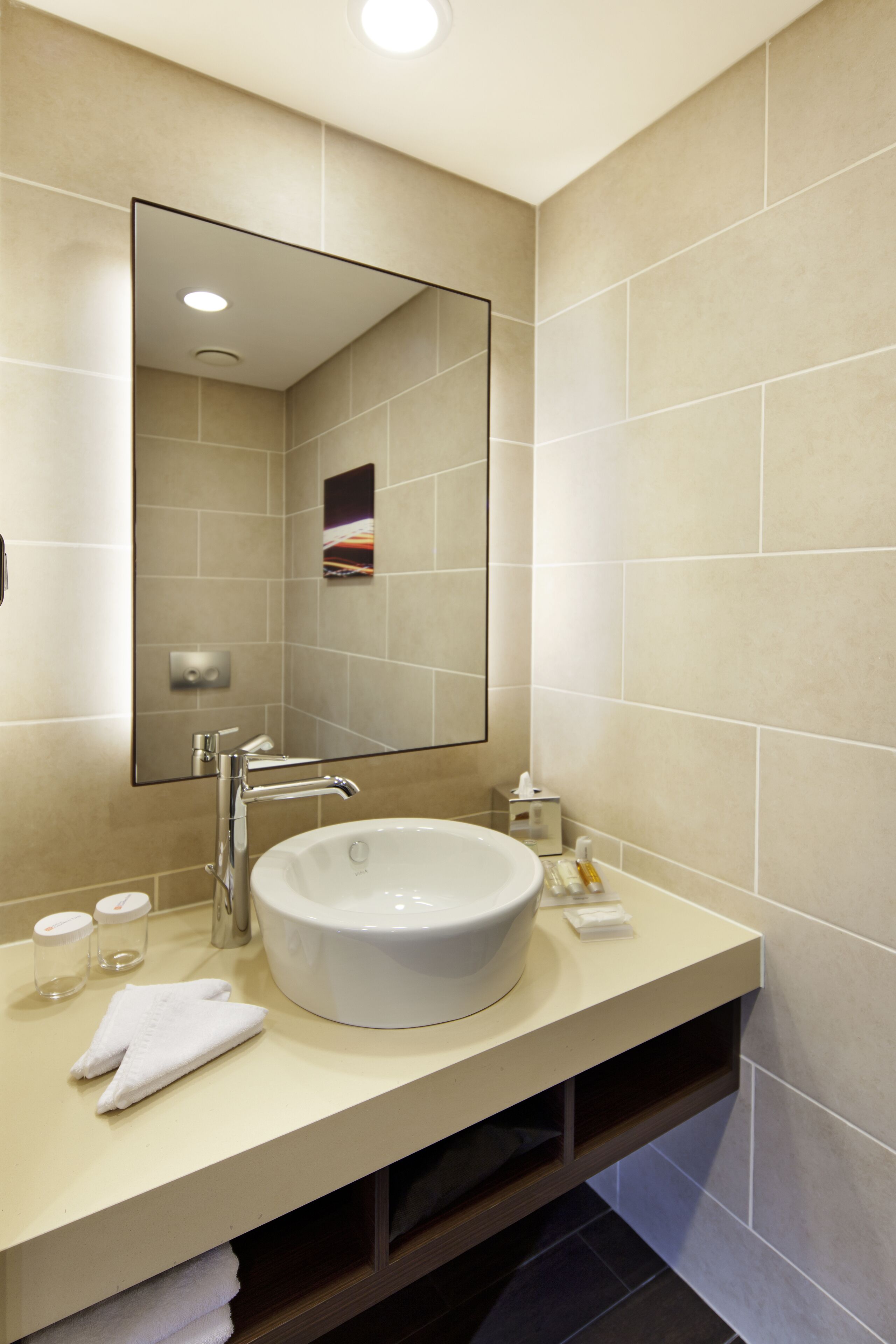 A modern bathroom with a large mirror, a white sink, and a beige countertop.