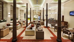 A spacious lobby with multiple seating areas, a central column, and a television mounted on the wall. - Hilton Garden Inn Mardin (Mardin)