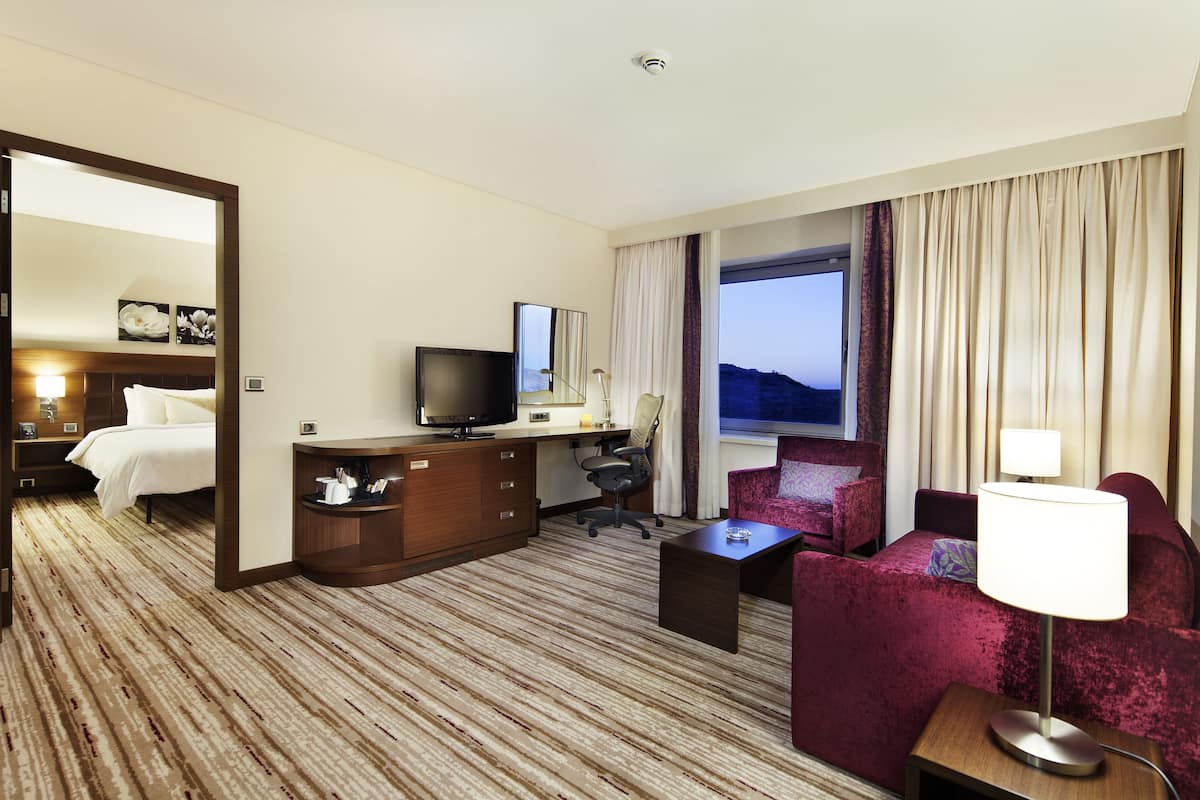 A hotel room with a bed, a desk with a TV, a chair, a sofa, and a lamp.
