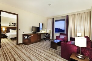 Una habitación de hotel con una cama, un escritorio con televisor, una silla, un sofá y una lámpara.