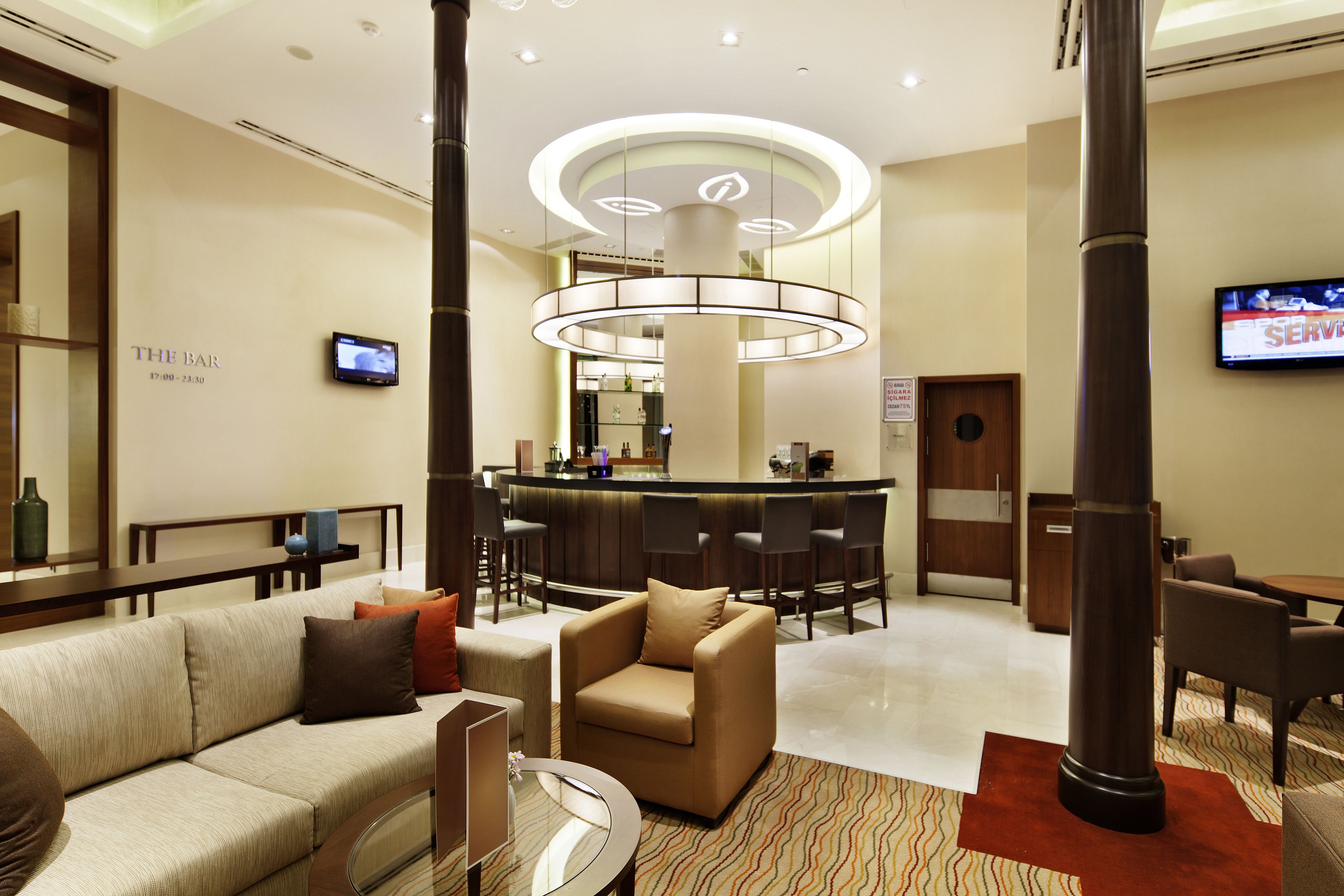 Een hotellobby met een bank, fauteuil en een bar met een televisie.