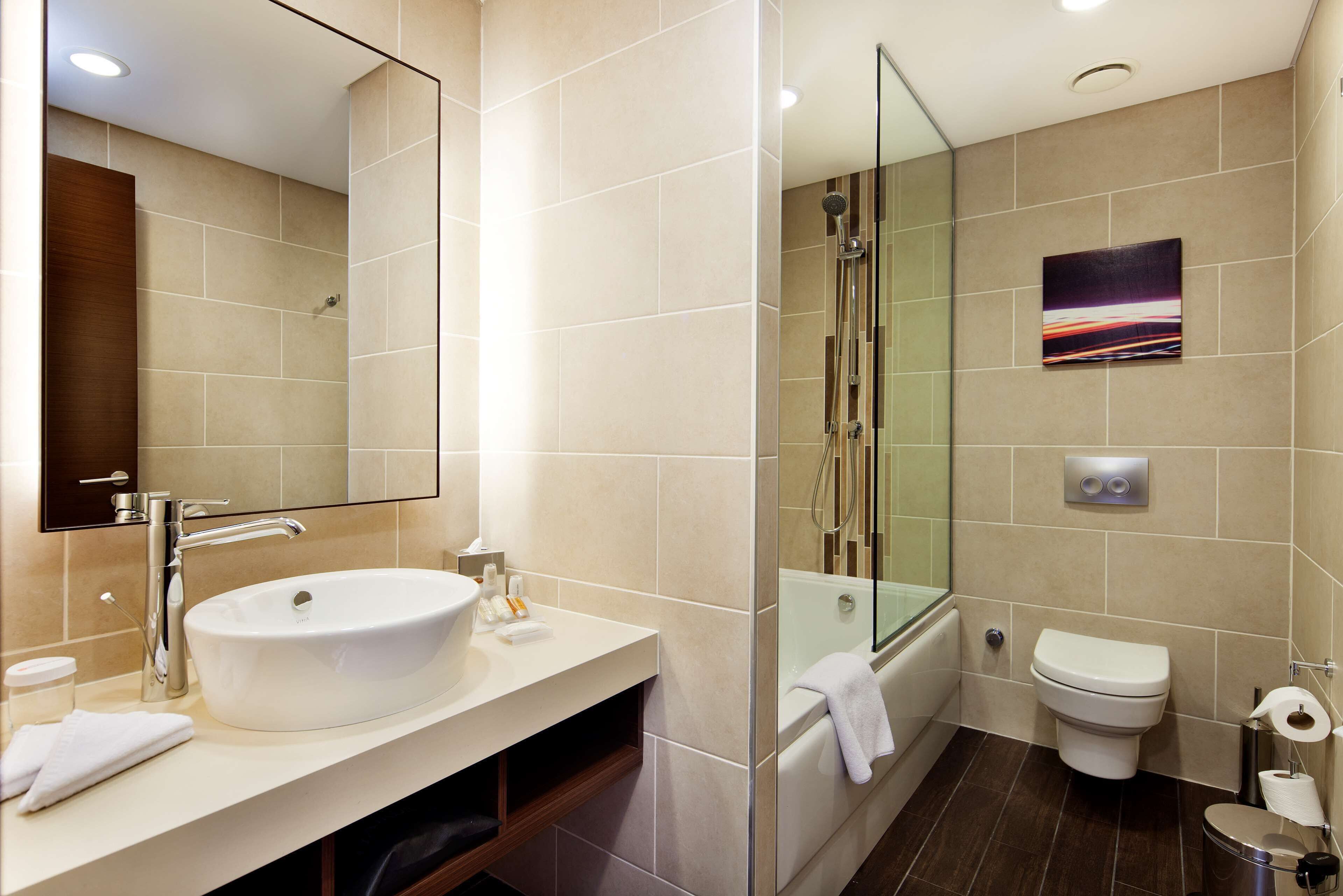 A modern bathroom with a large sink, a glass shower enclosure, a toilet, and a mirror.