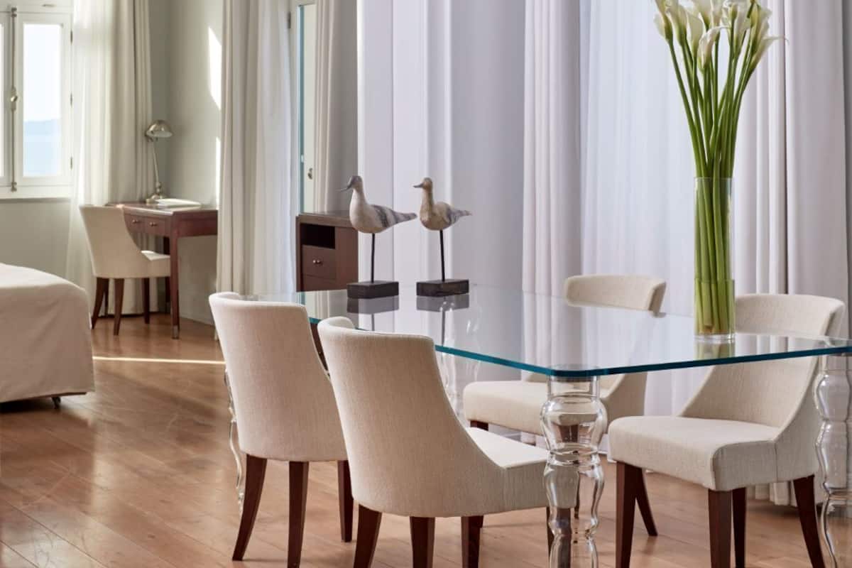 Ein modernes Hotelzimmer mit einem Glastisch, weißen Stühlen, einem Schreibtisch und einem Bett.