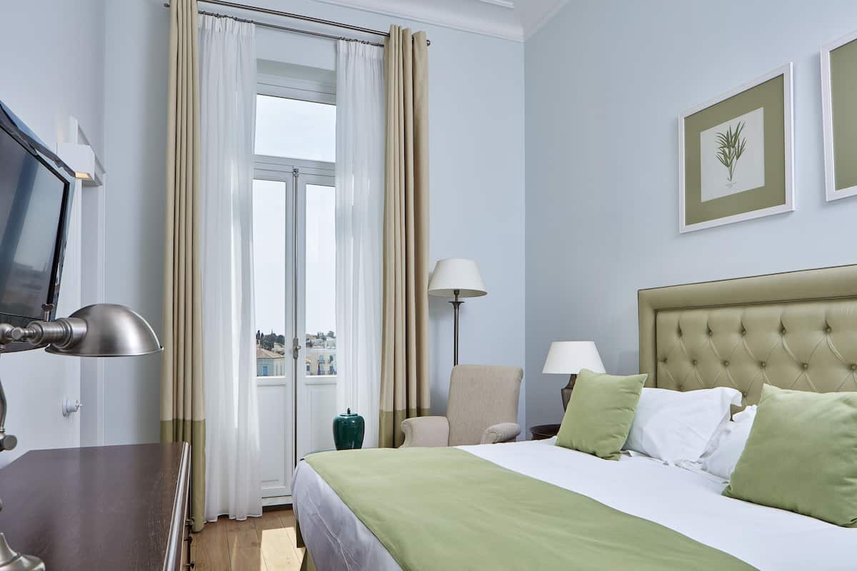 Ein Hotelzimmer mit Bett, Stuhl, Schreibtisch, Fernseher und einem Fenster mit Vorhängen.
