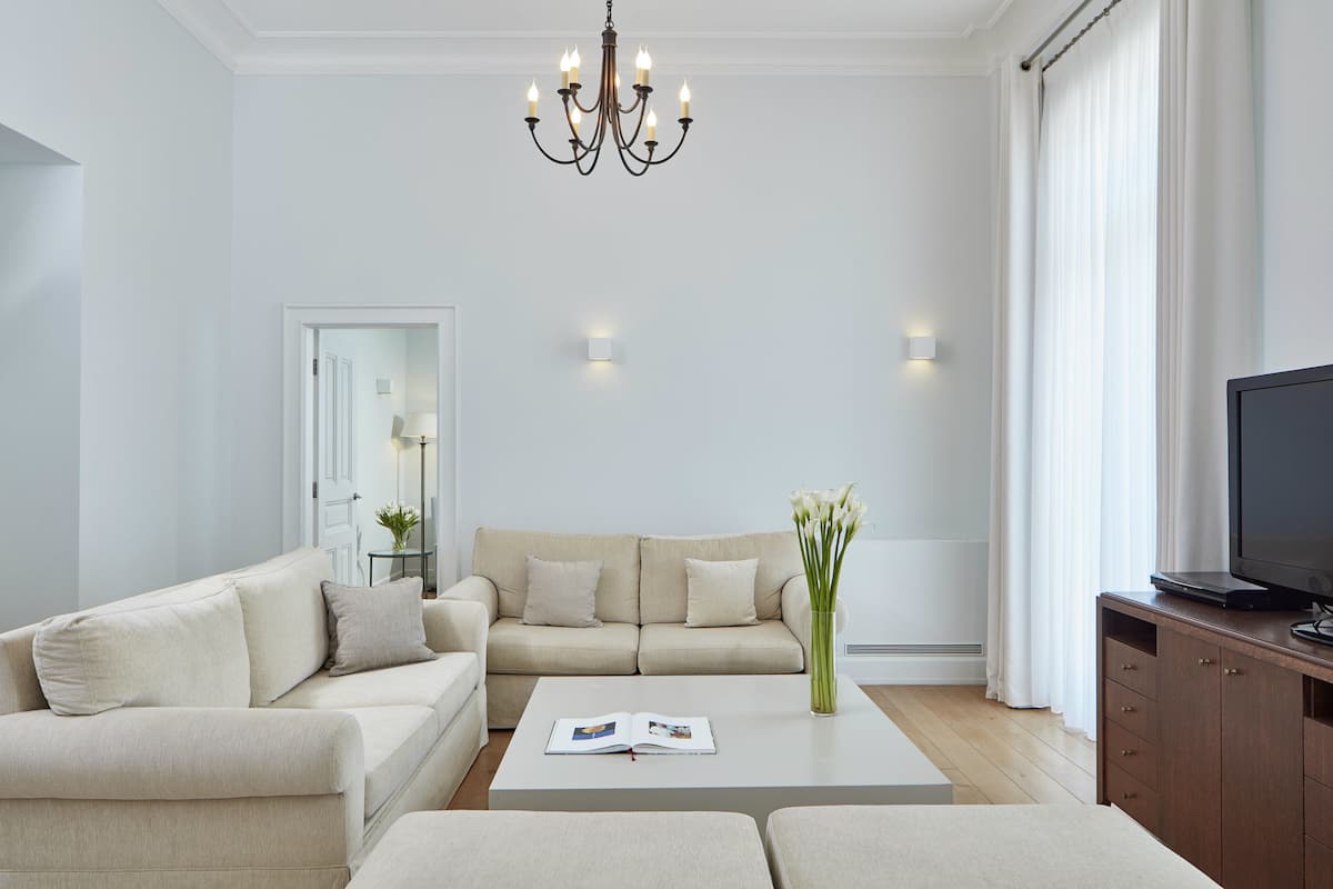 Ein modernes Wohnzimmer mit einem beige farbenen Sofa, einem Couchtisch mit einer Zeitschrift, einer Vase mit Blumen, einem Fernseher auf einer Holzkommode und einer Deckenleuchte.