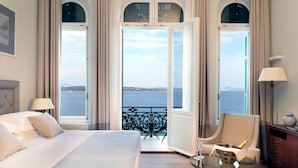 A hotel room with a bed, a chair, a small table with a bottle and glasses, and a balcony with a view of the sea. - Poseidonion Grand Hotel (Spetses)