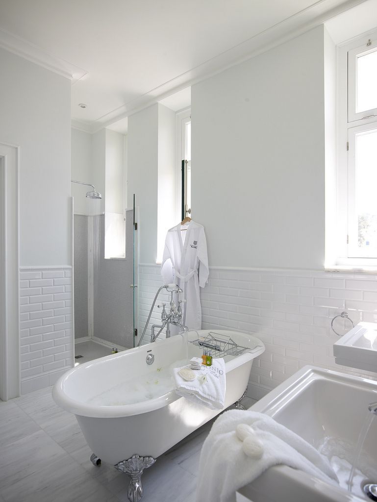 Een moderne badkamer met een vrijstaand bad, een douche met glazen wanden en een vloer betegeld met witte tegels.