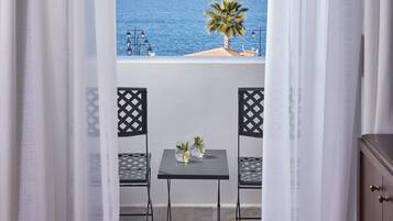 A balcony with a table and chairs, overlooking a coastal view with a palm tree and the sea.