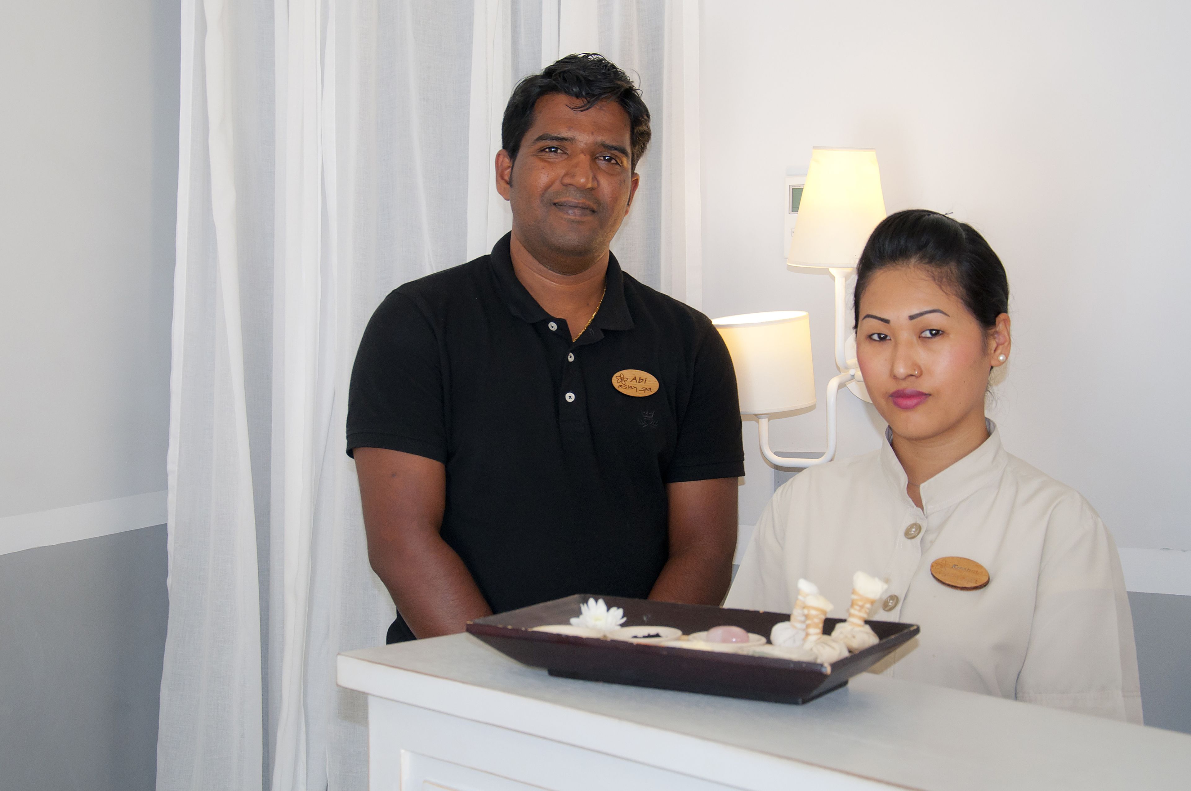A hotel reception desk with a man and a woman standing behind it, a name tag on the man's shirt, and a tray with food items.