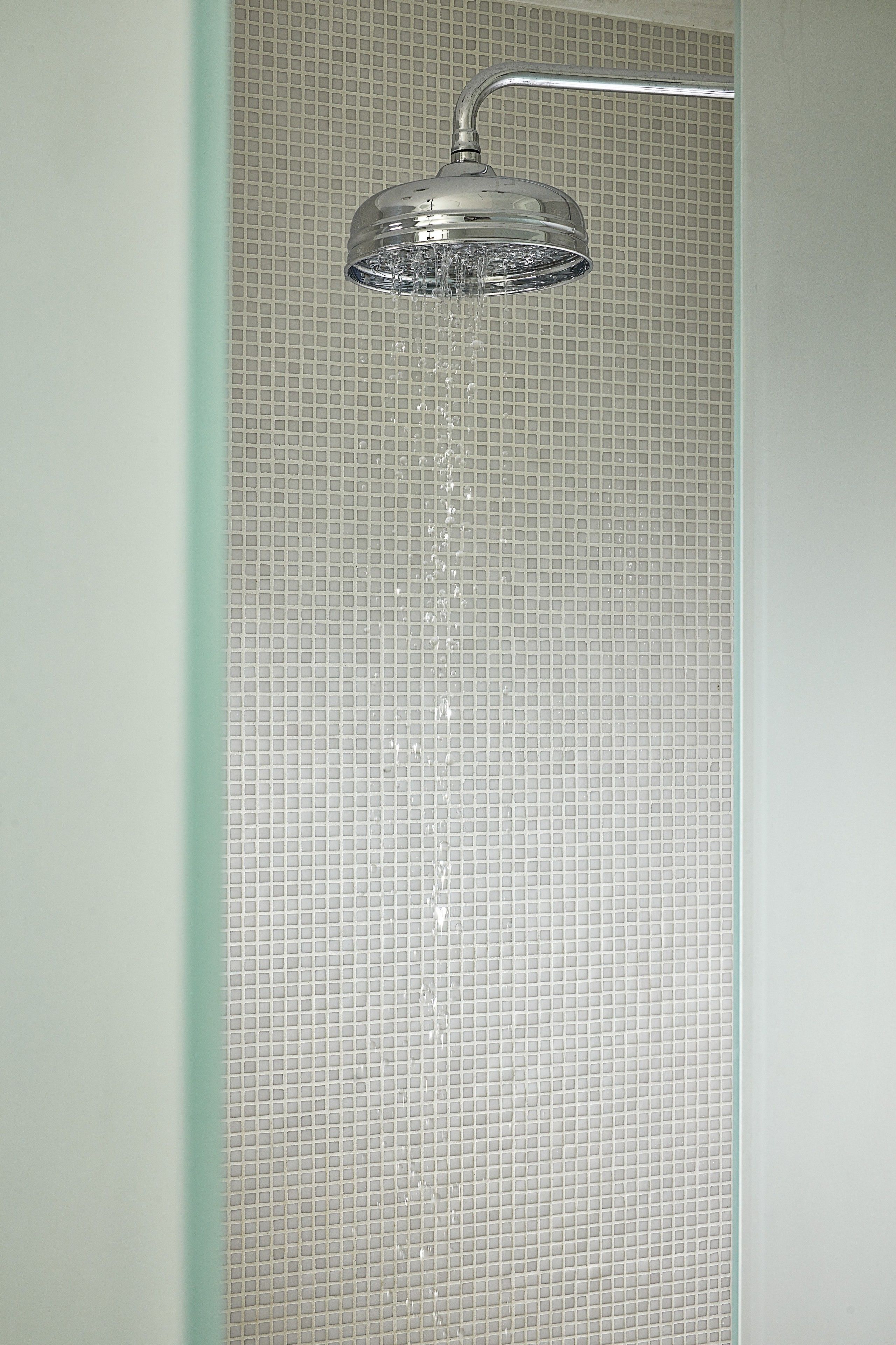 Une douche au design moderne, avec un motif de carreaux carrés sur le mur et une pomme de douche chromée.